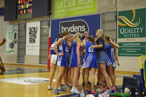 The netball team put their hands in a team huddle.
