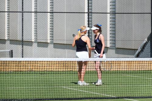 Two student athletes confer behind the net on a tennis court.
