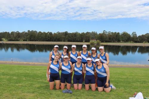 The rowing team poses for a photo in front of a lake